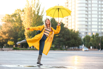 Beautiful young woman with umbrella wearing raincoat outdoors