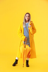 Beautiful young woman in raincoat and with umbrella on color background
