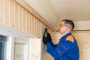 side view of a master in blue special clothing screwing a board beam with a screwdriver