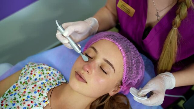 Cosmetology. Woman in clinic receiving stimulating electric facial treatment. Closeup of young female face during microcurrent therapy.