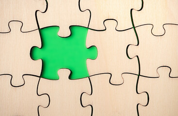 Missing puzzle piece. Almost finished, large jigsaw puzzle made of wood on green background. Concept for moving forward, understand a complicated process or filled in gaps of knowledge