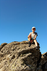boy sitting on the edge of a large rocky rock, summer hike in the mountains, the top of the mountain.
