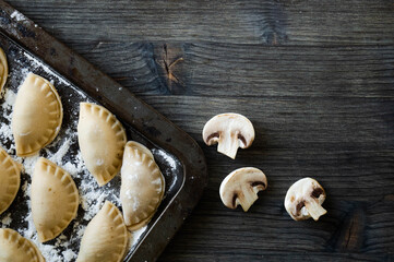 Russian dumplings with mushrooms dusted with floor on the dark wooden background