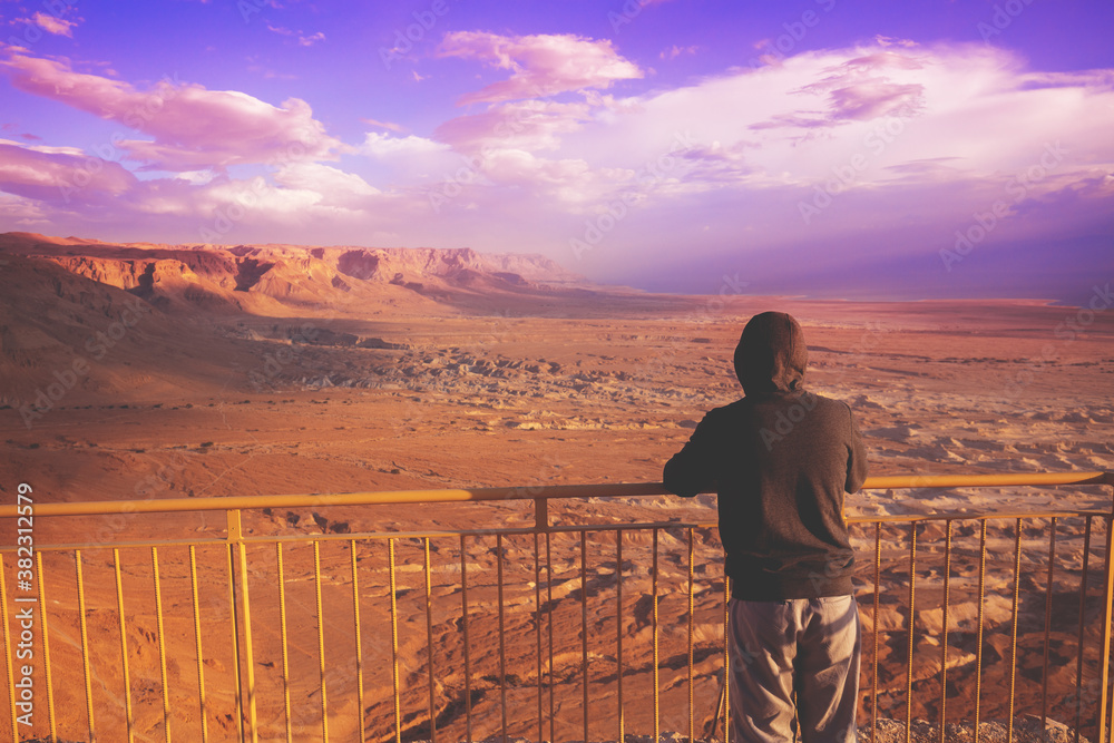 Wall mural young man standing on a viewpoint on the mount (masada) and gazing sunrise in the desert. the man lo