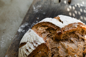 Half of homemade whole grain wheat and rye bread dusted with flour on the vintage wooden pan