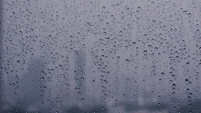 Footage of rain drop on glass window with blurred city background.