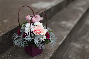 A bouquet of flowers: roses and chrysanthemums in a gift box against a background of rough cement