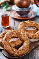 Freshly baked simit baked goods with sesame seeds close-up (Turkish bagel - Gevrek or Kuluri). Traditional white bread with sesame seeds for breakfast, a glass of armudu with red tea on a wooden table