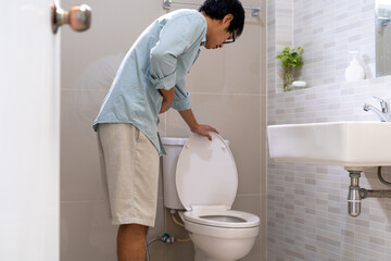 An Asian man in front of the toilet has severe abdominal pain. The man is having diarrhea in the...