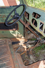 The ground is visible through the floorboard of an abandoned antique truck