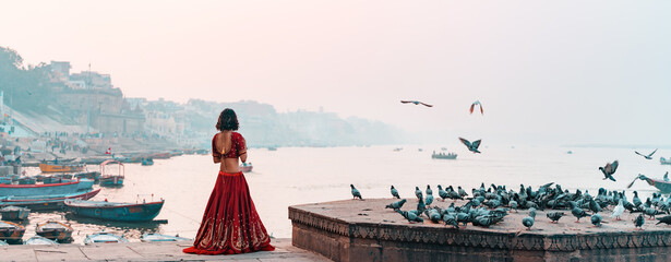 A beautiful Indian woman in a red Sari stands alone on the street. There is a flock of pigeons on...