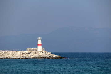 Lighthouse tower on a stone pier in azure sea against misty mountains