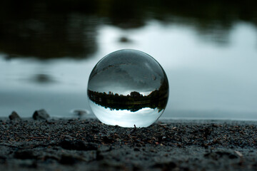 A transparent lens ball on a lake shore by the water. Lakeshore view through the lens ball.