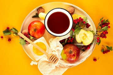 Cozy autumn hot spiced tea with honey, apples and red hawthorn berries on a tray. Still life on an orange background. Flat lay