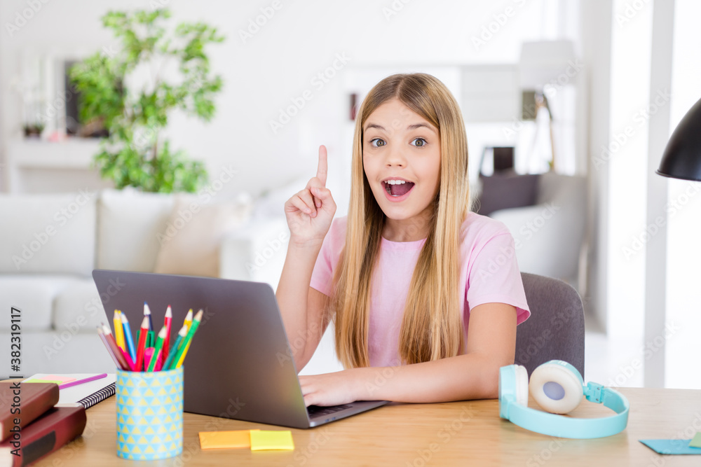 Canvas Prints Photo of shocked little kid girl sit cozy table use laptop think thoughts solve home work task raise index finger up in house indoors