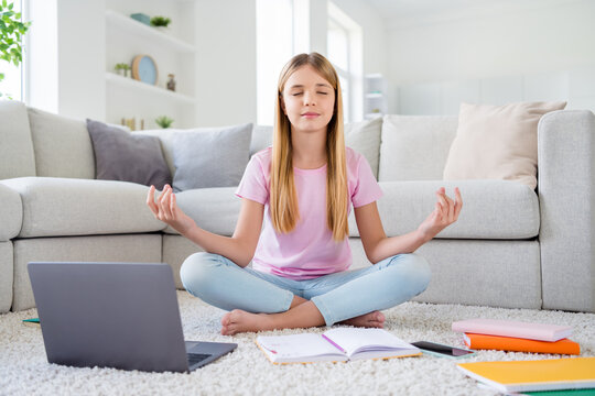 Full length photo of focused kid girl study remote sit floor carpet legs crossed close eyes meditate practice balance before e-learning lesson in house indoors