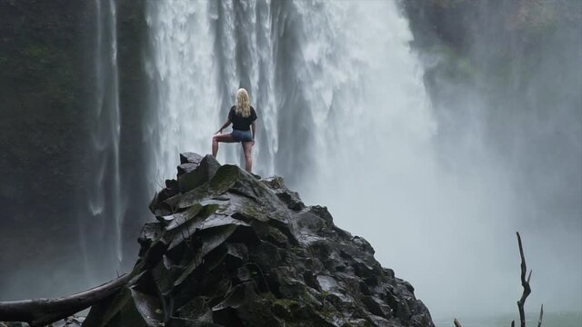 Beautiful blond female model looking at waterfall in slow motion shot