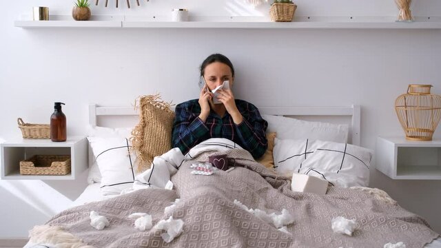 Young Woman with Flu Talking on Phone while Lying in Bed and Drinking Tea. Female in Pajamas Looking at Thermometer at Home. Seasonal Infections, Virus, Cold and Flu Concept