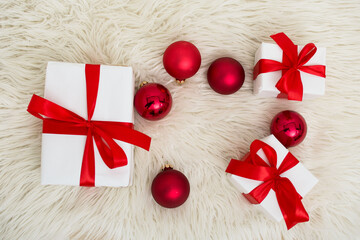 White Christmas gift boxes with red ribbon and Christmas balls on furry blanket. Flat lay. Top view...