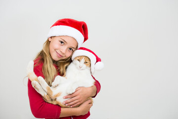 Pretty young girl with cat  with santa claus hat. Child in red santa hat holding cat. Christmas animal concept, copy space.
