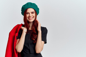 Naklejka premium A woman holds in her hand a red coat and a dark T-shirt Green hat cropped view of a light background