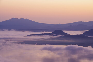 湖を覆う朝靄と山々のシルエット。北海道、津別峠からの夜明けの風景。