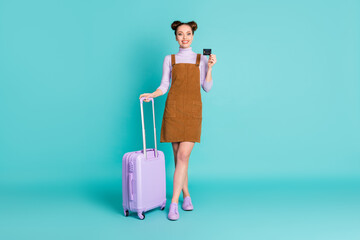 Full body photo of attractive cheerful positive two buns lady passenger pay for international travelling plastic card hold lilac luggage wear spring outfit isolated turquoise color background