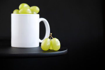 Green grapes portion inside a white mug on black background