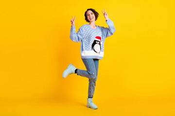 Full length photo of attractive cute lady x-mas party good mood greet friends show v-sign symbol wear penguin ugly ornament sweater jeans shoes isolated yellow shine color background