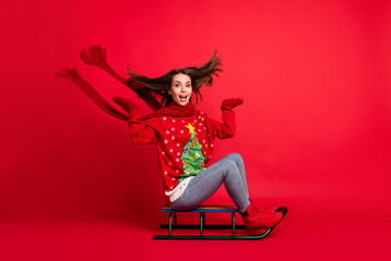 Full length body size profile side view of her she attractive cheerful cheery girl sitting riding sledge having fun spending vacation season isolated bright vivid shine vibrant red color background