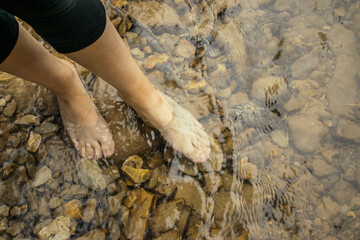Women feet standing in the clear water of forest river