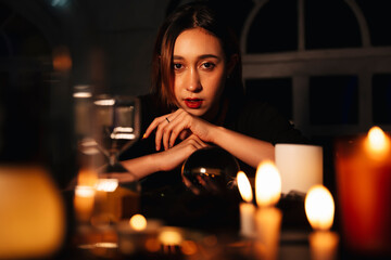 Beautiful long hair woman fortune teller with crystal ball in dark room.