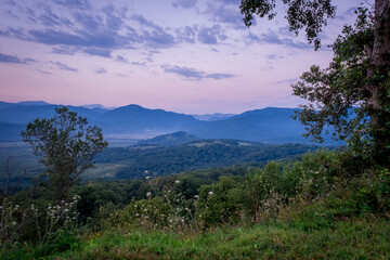 Early morning one hour before dawn. Silhouettes of mountains in the morning haze, grass and trees in the foreground. Lagonaki Plateau, Republic of Adygea, Russia