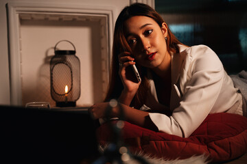 Woman having conversation on the phone and looking at laptop computer in bedroom.