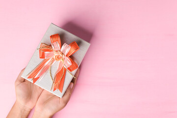Gift box with orange ribbon holding by hand on pink background, present for giving in special day, Top view