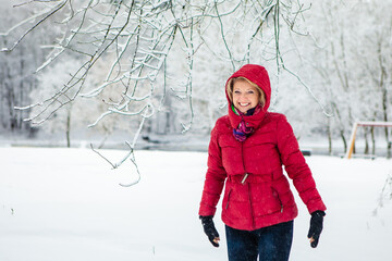 Caucasian white woman with red jacket enjoying playful on snowy day with blurry white forest background.Christmas time. Happiness. Snowfalls.