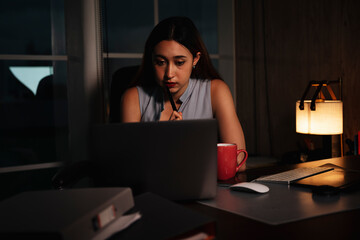 Beautiful woman working overtime on laptop computer at night.