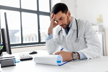 healthcare, medicine and people concept - stressed male doctor with clipboard at hospital