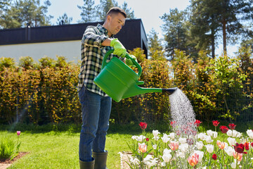 gardening and people concept - middle-aged man with watering can pouring water to flower bed at...