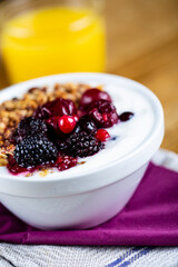 Delicious bowl filled with fresh berries and yogurt. Orange juice glass in background. Selective focus on subject.