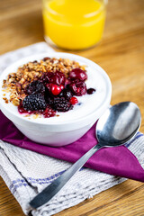 Delicious bowl filled with fresh berries and yogurt. Orange juice glass in background. Selective focus on subject.