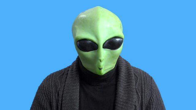 Blogger in funny alien costume and home outfit sits in front of camera to record video to create interesting entertainment content for vlog. Themed costume for party. Gesture of fright or surprise.