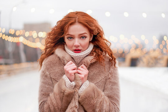 Young beautiful redhead girl freckles ice rink on background. Pretty woman curly hair portrait walking on new year fair