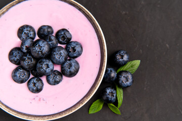 Tasty fresh blueberry yoghurt shake dessert in ceramic bowl standing on black dark table background.