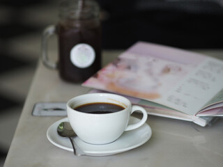 espresso Black coffee in a white cup placed with clear glass menu book on marble table