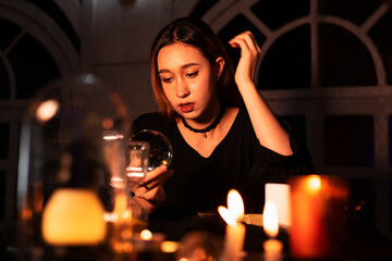 Beautiful young woman fortune teller looking at crystal ball to predict the future.