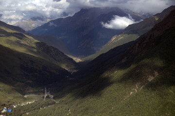 Green valley and mountains. Green hills in a mountain landscape with light rays passing through the clouds. Mountain peaks covered with snow. Caucasus, Russia.