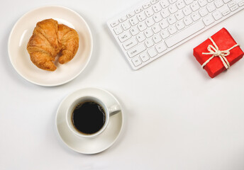 flat lay of coffee cup ,croissant ,computer keyboard and red gift box on white background with copy space. Seasonal holiday and workplace.