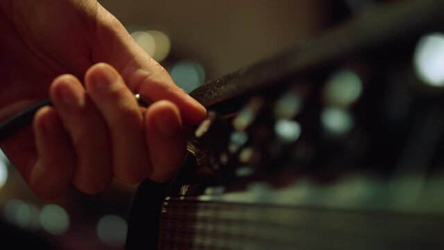 Sound engineer hand connecting plug to amplifier in late night recording studio.