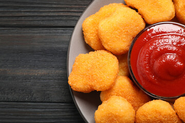Tasty fried chicken nuggets with tomato sauce on black wooden table, top view